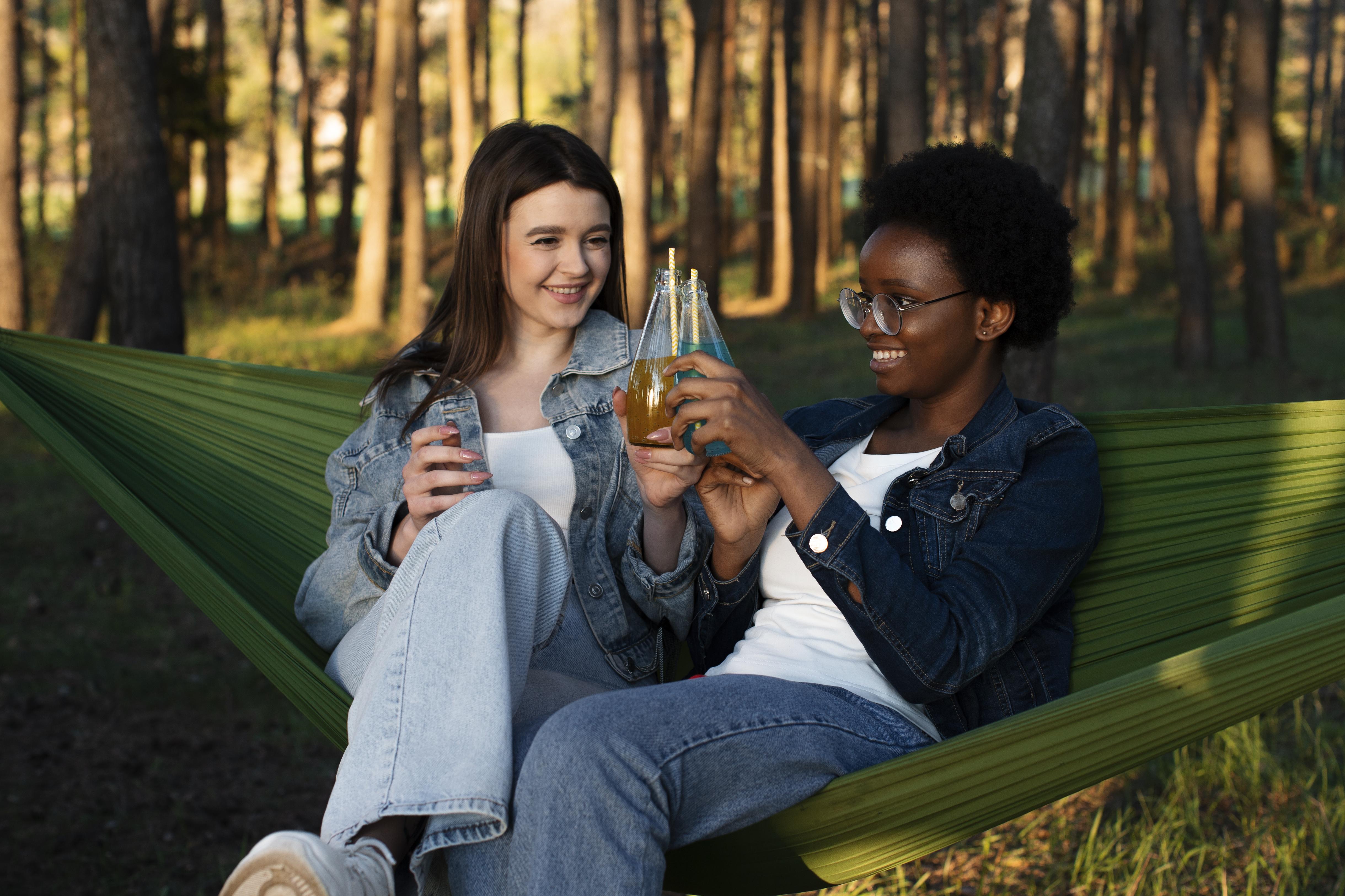 Two friends sharing drinks and relaxing in a hammock in natural afternoon light